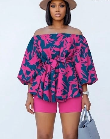 The Bloom Two-Piece Set is confidence in print form. A vibrant hot pink floral pattern bursts across a deep navy off-shoulder peplum top with voluminous balloon sleeves — cinched at the waist with a matching belt tie and paired with solid hot pink biker shorts that complete the look with intention.