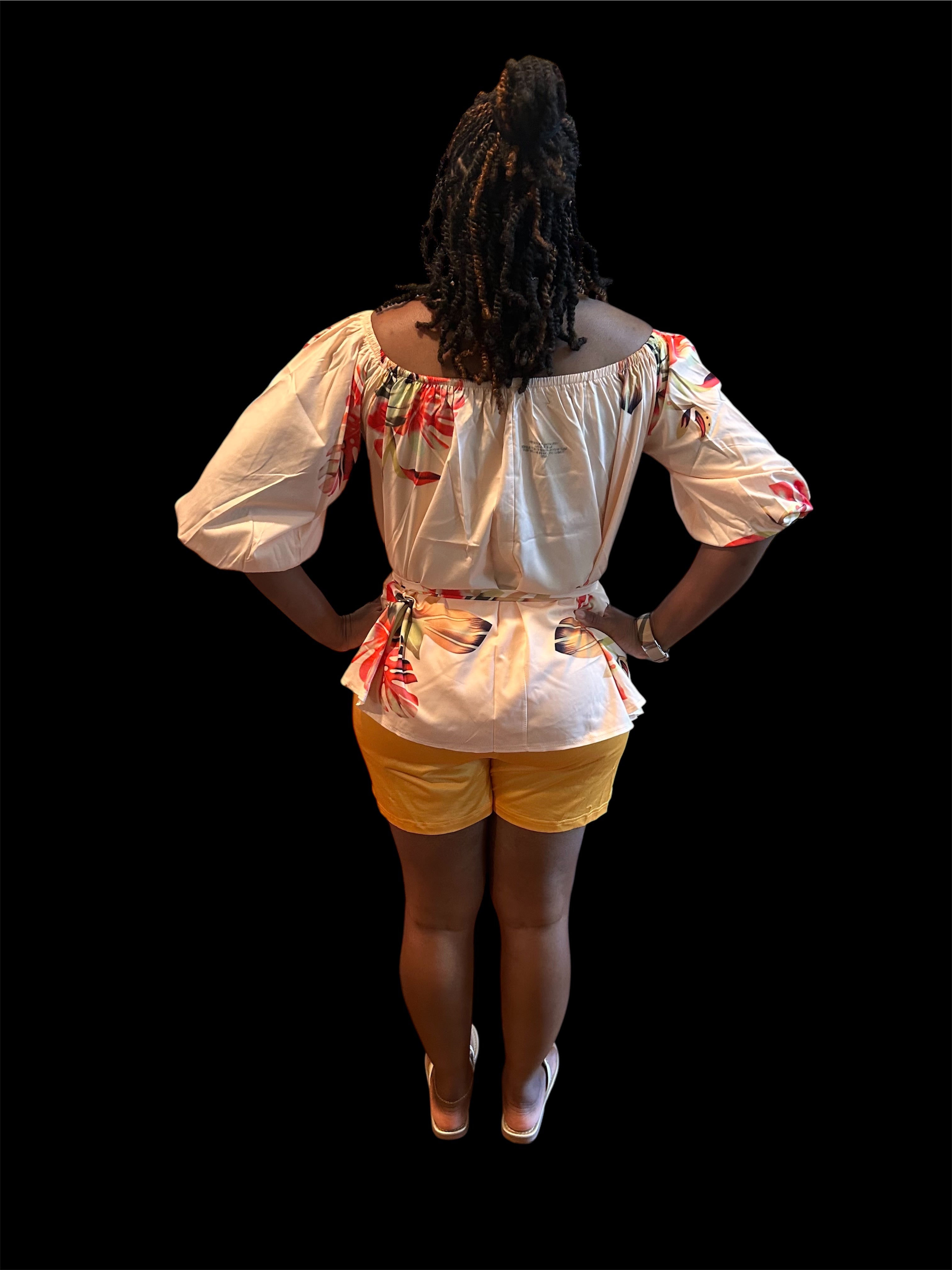The Golden Hour Two-Piece Set is the calm confidence of a perfect moment — bottled in fabric. A warm champagne base blooms with coral, green, and red tropical florals across an off-shoulder peplum top with soft balloon sleeves — cinched with a matching belt tie and paired with rich gold biker shorts that glow against every skin tone.