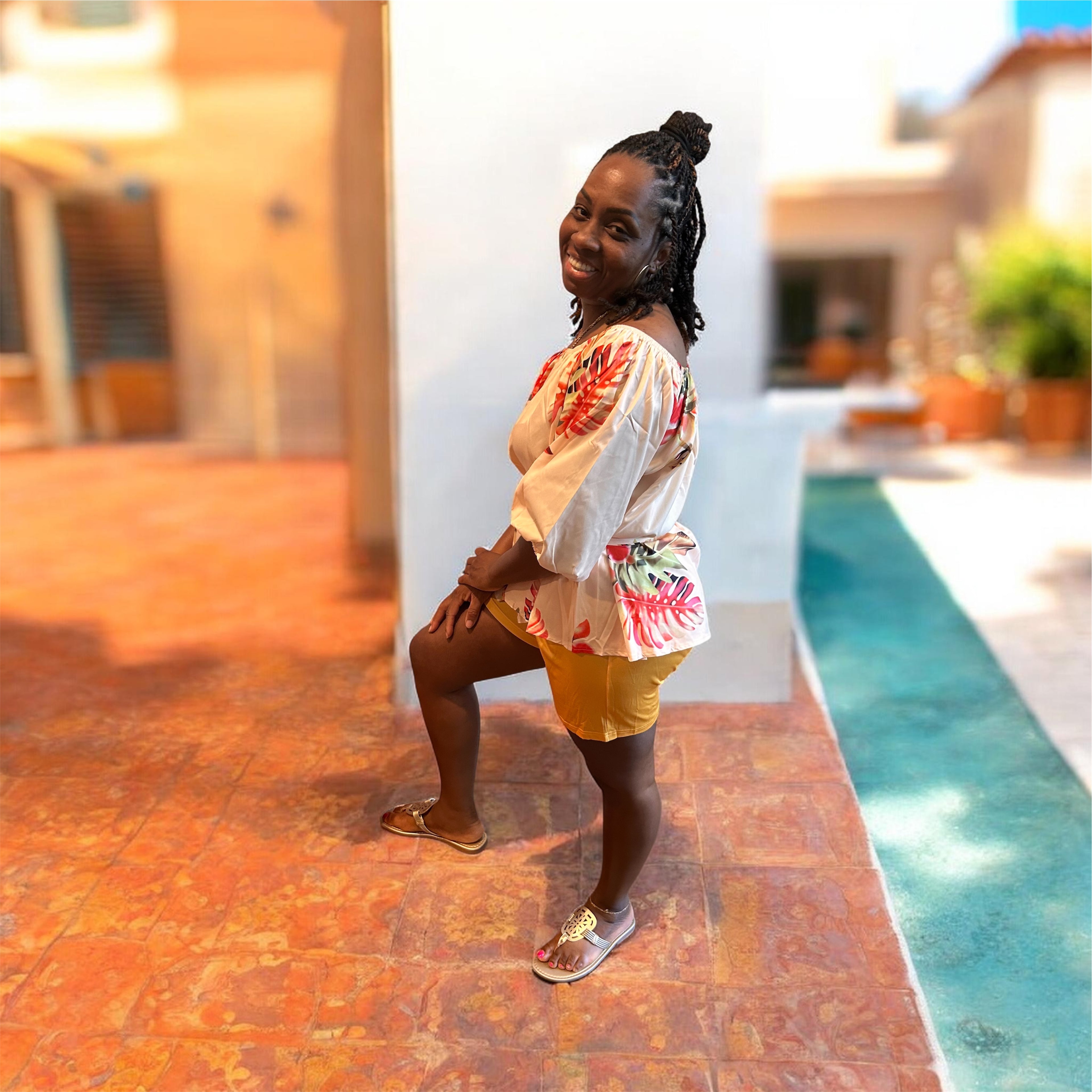 The Golden Hour Two-Piece Set is the calm confidence of a perfect moment — bottled in fabric. A warm champagne base blooms with coral, green, and red tropical florals across an off-shoulder peplum top with soft balloon sleeves — cinched with a matching belt tie and paired with rich gold biker shorts that glow against every skin tone.