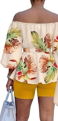 The Golden Hour Two-Piece Set is the calm confidence of a perfect moment — bottled in fabric. A warm champagne base blooms with coral, green, and red tropical florals across an off-shoulder peplum top with soft balloon sleeves — cinched with a matching belt tie and paired with rich gold biker shorts that glow against every skin tone.