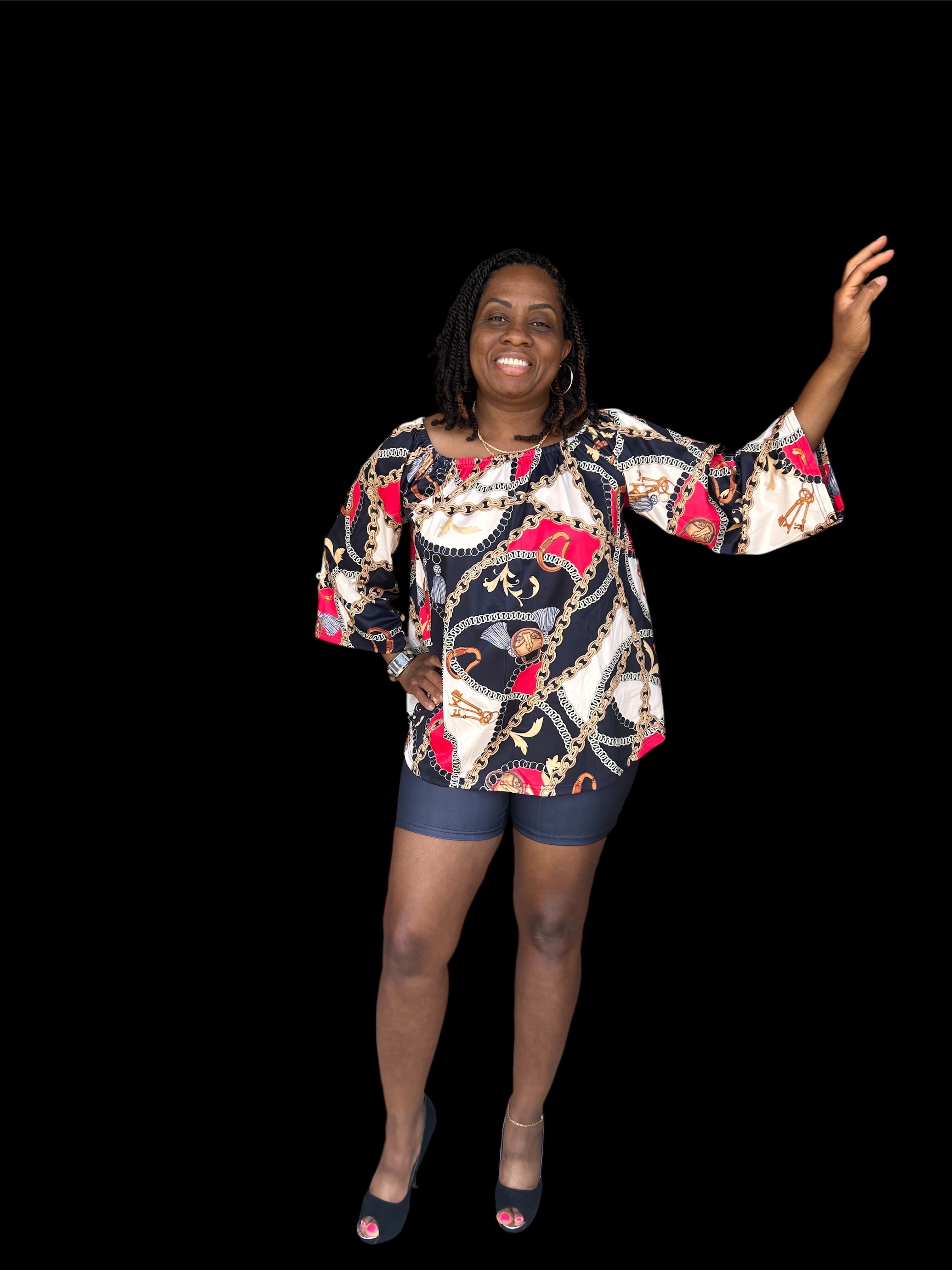 The Reign Two-Piece Set isn’t for blending in. A bold chain-and-medallion heritage print in gold, burgundy, and black drapes across an oversized off-shoulder peplum top — cinched with a matching belt tie and paired with sleek black biker shorts that anchor the look with intention.