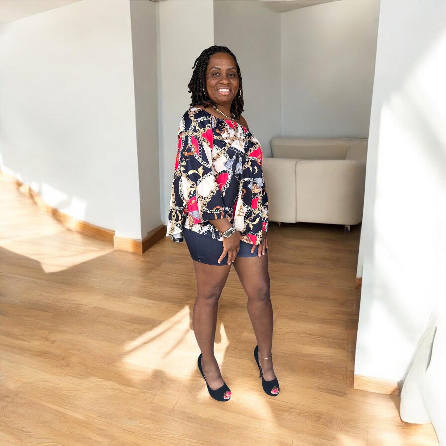 The Reign Two-Piece Set isn’t for blending in. A bold chain-and-medallion heritage print in gold, burgundy, and black drapes across an oversized off-shoulder peplum top — cinched with a matching belt tie and paired with sleek black biker shorts that anchor the look with intention.