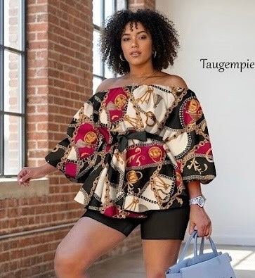 The Reign Two-Piece Set isn’t for blending in. A bold chain-and-medallion heritage print in gold, burgundy, and black drapes across an oversized off-shoulder peplum top — cinched with a matching belt tie and paired with sleek black biker shorts that anchor the look with intention.