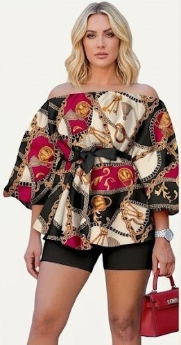 The Reign Two-Piece Set isn’t for blending in. A bold chain-and-medallion heritage print in gold, burgundy, and black drapes across an oversized off-shoulder peplum top — cinched with a matching belt tie and paired with sleek black biker shorts that anchor the look with intention.