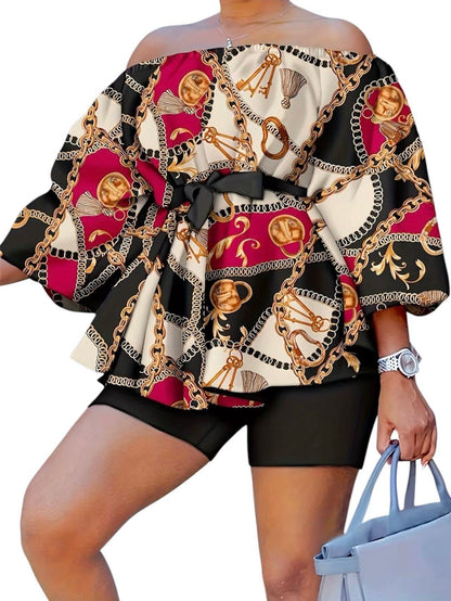 The Reign Two-Piece Set isn’t for blending in. A bold chain-and-medallion heritage print in gold, burgundy, and black drapes across an oversized off-shoulder peplum top — cinched with a matching belt tie and paired with sleek black biker shorts that anchor the look with intention.