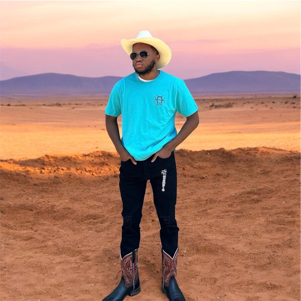 The Mark Crew in Blue doesn’t blend into the background — it owns it. A striking turquoise 100% cotton crewneck carries the TAUGEMPIE crest mark on the left chest and the full signature logo graphic across the back in vivid blue, green, and gold.
