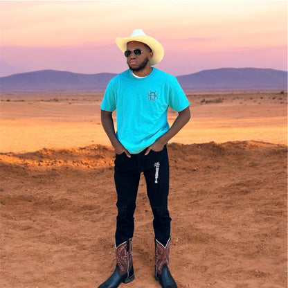 The Mark Crew in Blue doesn’t blend into the background — it owns it. A striking turquoise 100% cotton crewneck carries the TAUGEMPIE crest mark on the left chest and the full signature logo graphic across the back in vivid blue, green, and gold.
